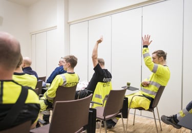 Medlemmar i Elektrikerna iklädda varselkläder sitter på stolar i ett mötesrum under ett pågående medlemsmöte