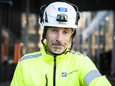 Elektriker i varselklädder och skyddshjälm som tittar in i kameran och ler