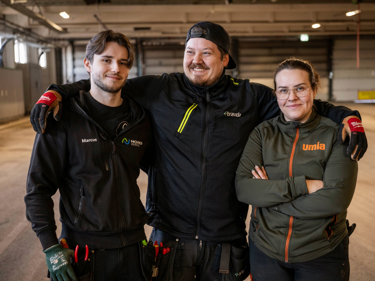 Tre unga elektriker som står bredvid varandra med armarna på varandras axlar