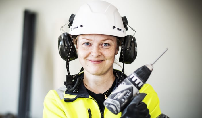 Leende elektriker i som befinner sig på ett bygge och håller en skruvdragare i handen