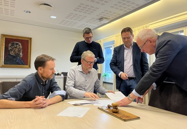 Fem män som befinner sig i ett konferensrum och som tillsammans signerar papper